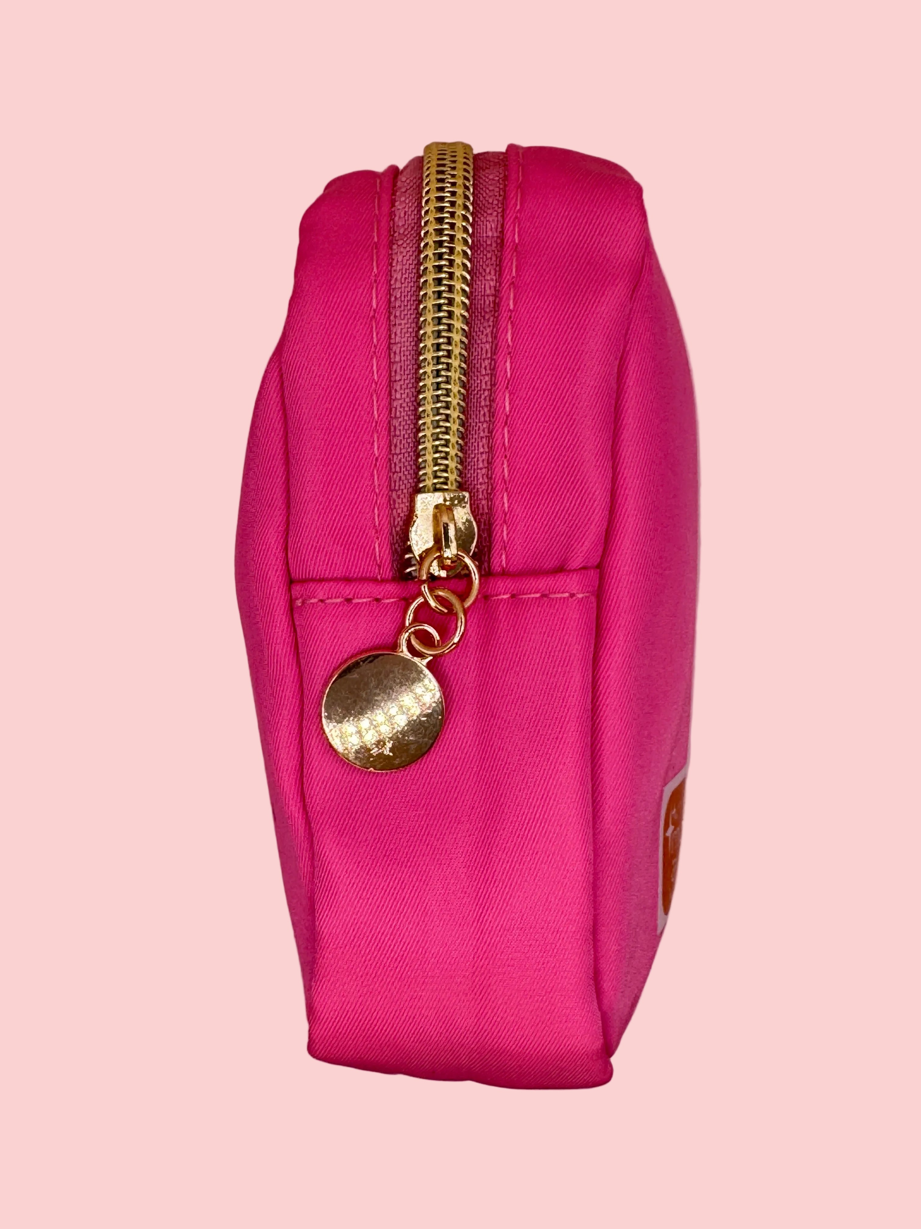 Pink pouch with a gold zipper and decorative charm on a pink background