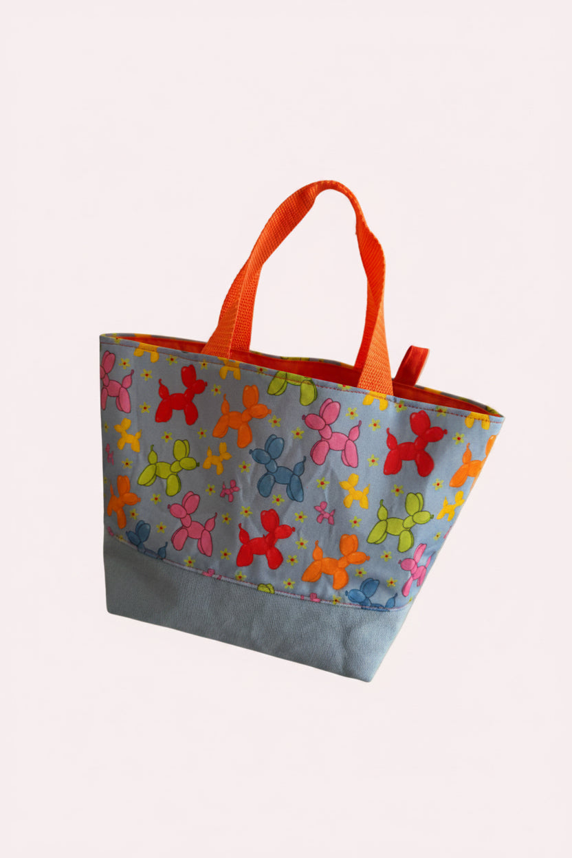 Colorful bag with balloon dog pattern held by a hand against a white door.
