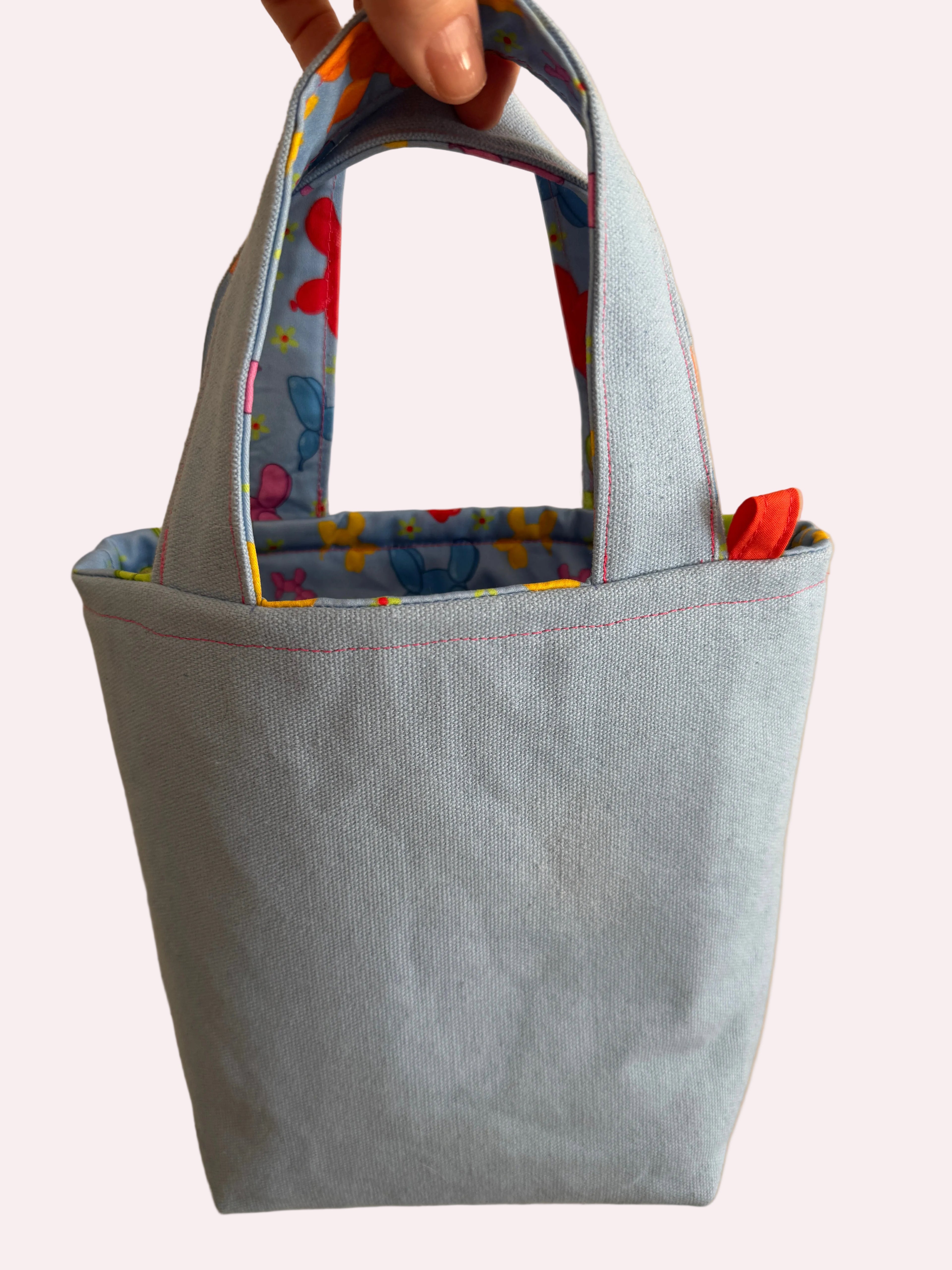 Light blue tote bag with colorful handles held by a hand on a beige background