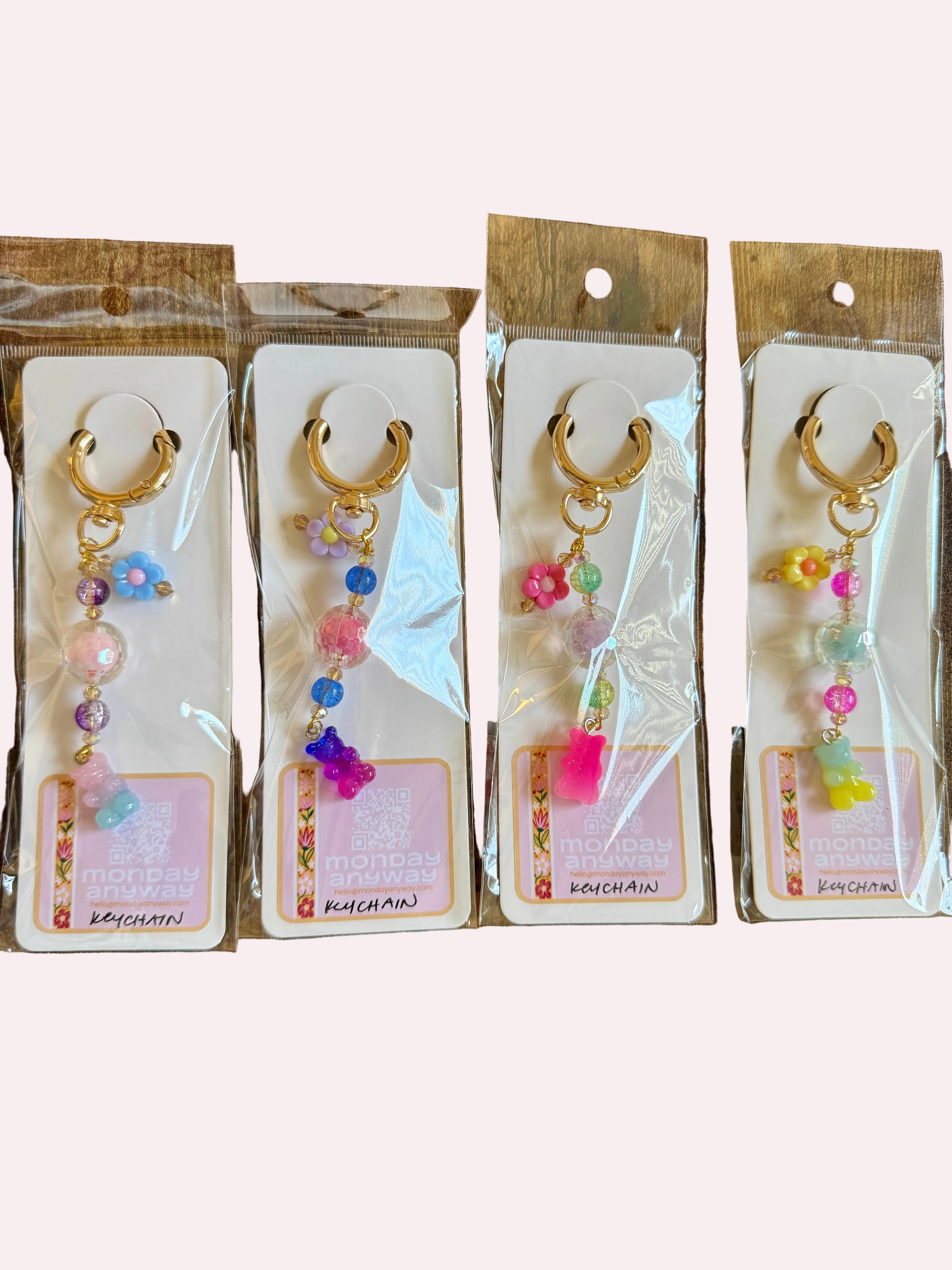 Four pairs of decorative keychain/charms in clear packaging on a wooden surface.