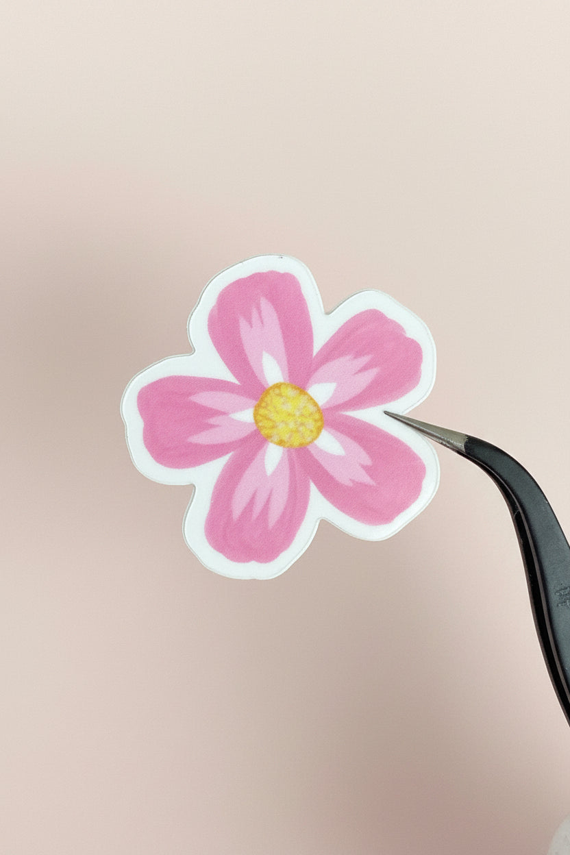 Pink flower sticker being held by tweezers on a wooden surface