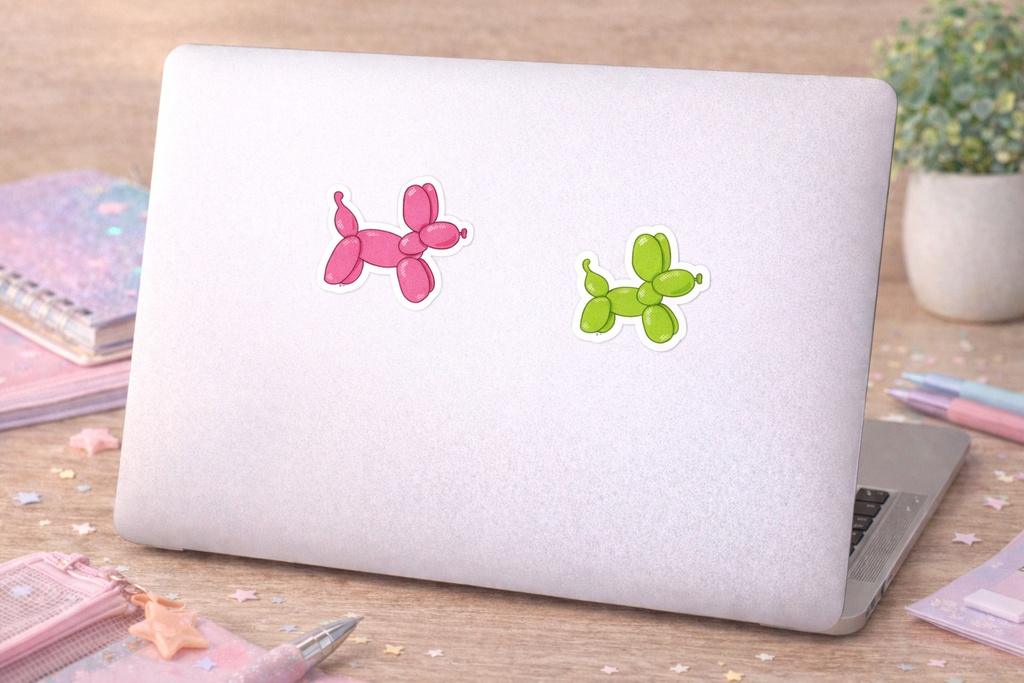 Laptop with pink and green balloon dog stickers on a wooden surface