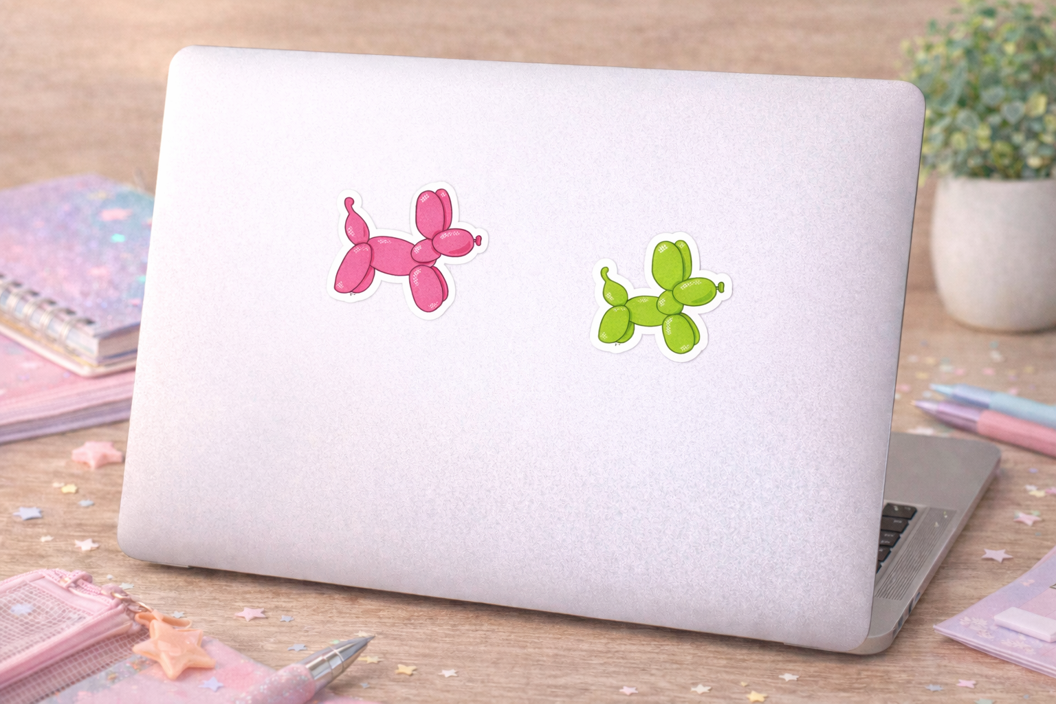 Laptop with pink and green balloon dog stickers on a wooden surface